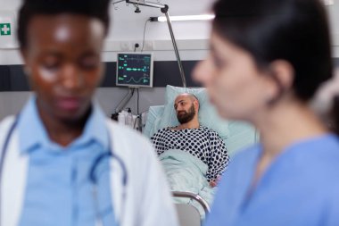 Siyahi tenli pratisyen, hastane koğuşunda çalışan kadın hemşireyle iyileşme tedavisini tartışıyor.