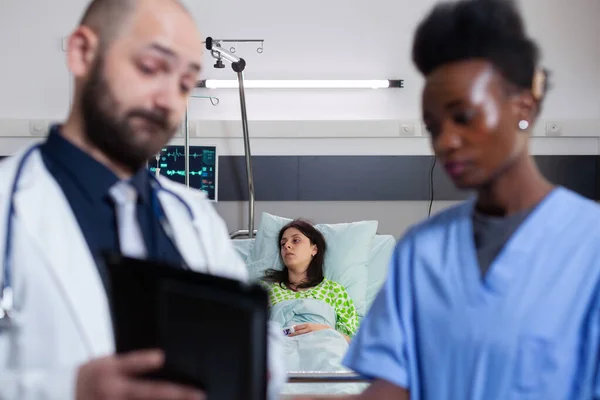 Practitioner doctor with black nurse checking recovery treatment using tablet computer