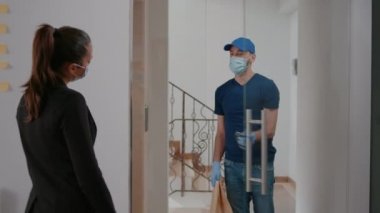 Üniformalı teslimatçı, koruma eldivenleri ve maskesiyle paket yemek siparişi veriyor.