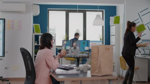 Femme entrepreneure assise au bureau dans un bureau d'entreprise en train de manger un sandwich lors d'une conférence en ligne sur vidéocall — Video