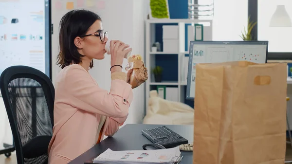 Zakenvrouw eten hapje smakelijke sandwich drinken koffie in de voorkant van monitor — Stockfoto