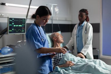 Doktor asistanı panoya not alırken Afrikalı doktor da kıdemli hastaya güvence veriyor.