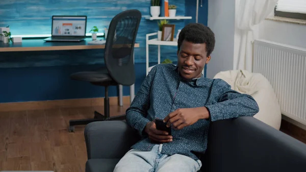 Hombre afroamericano con teléfono en las manos mirando contenido de servicios de streaming en línea —  Fotos de Stock