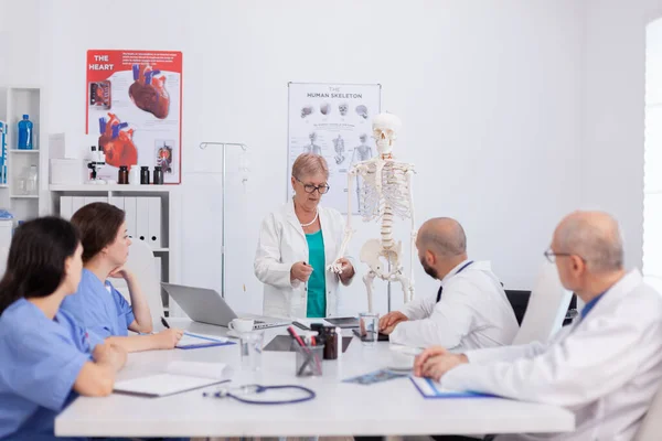 Médico mujer mayor sosteniendo estructura ósea discutiendo estructura humana — Foto de Stock