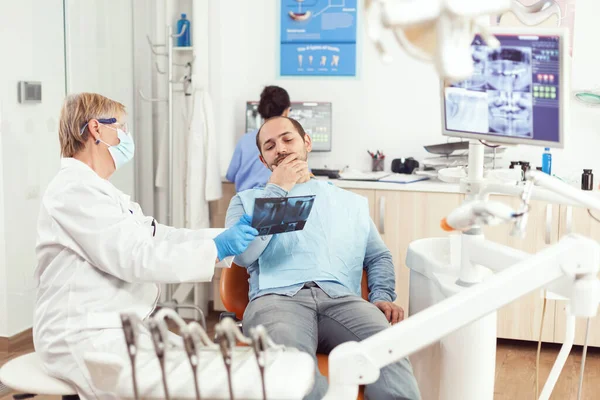Старшая стоматолог осматривает зубную рентгенографию с больным мужчиной — стоковое фото