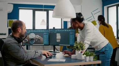 Çift monitörlü endüstriyel proje hakkında tartışan çok ırklı bir ekip