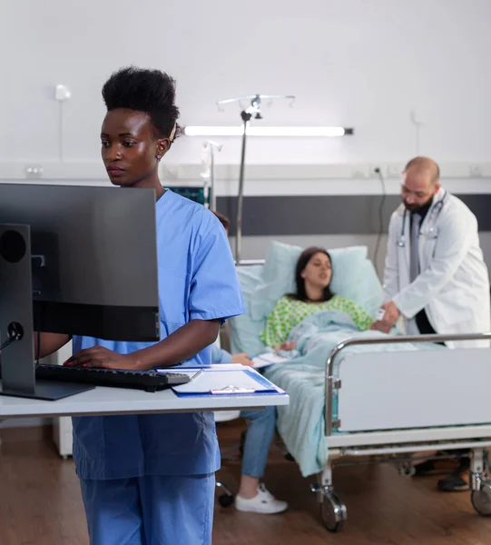 Czarna pielęgniarka wpisując objaw choroby, podczas gdy lekarz specjalista — Zdjęcie stockowe