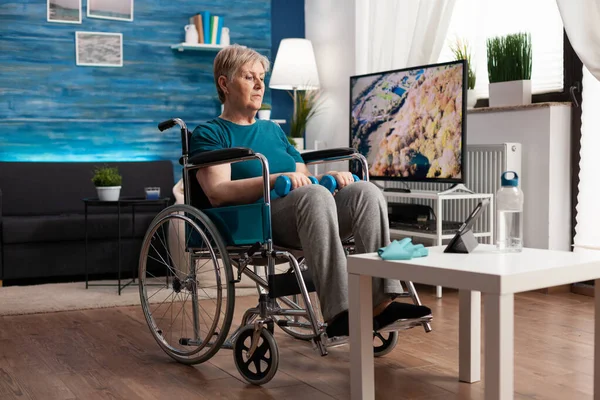 Femme âgée handicapée en fauteuil roulant regardant la vidéo en ligne gymnastique sur tablette — Photo