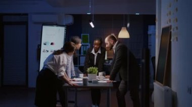 Çeşitli çok ırklı iş adamları konferans masasında duran grafikler üzerinde tartışıyor.