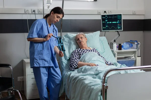 Medische verpleegkundige analyseert senior patiënt röntgenfoto 's in ziekenhuis kamer — Stockfoto