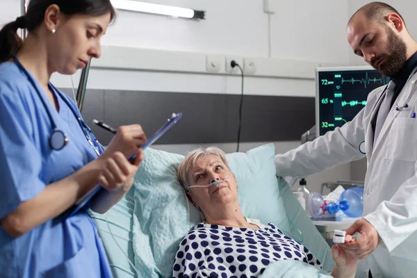 Malata donna anziana guardando il personale medico che posa nel letto d'ospedale — Foto Stock