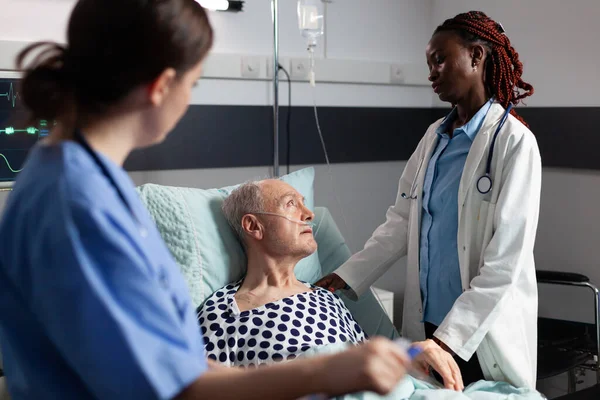 Afrikanischer Arzt im Krankenhauszimmer diskutiert mit krankem Senior — Stockfoto