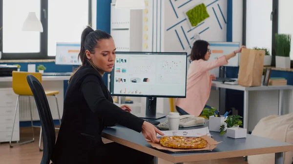 Zakenvrouw die lunchtijd eten afhaalpizza snijd aan het bureau in het kantoor — Stockfoto