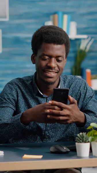 Hombre negro en la sala de estar disfrutando de contenido de redes sociales en el teléfono —  Fotos de Stock