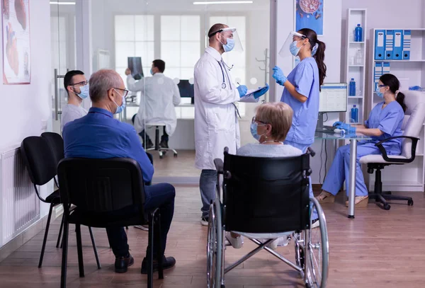 Arzt spricht mit Krankenschwester mit Mundschutz und Klemmbrett — Stockfoto