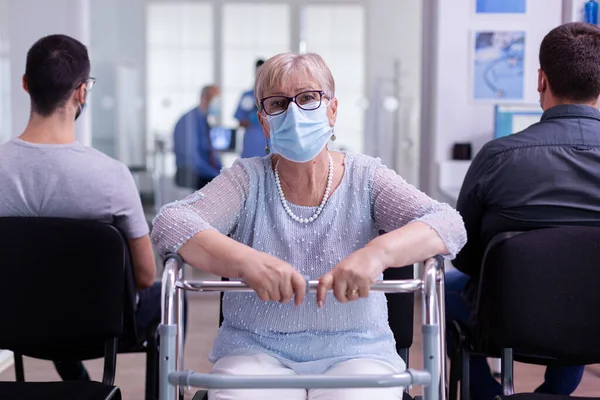 Anciano con marco para caminar sentado en la recepción del hospital mirando a la cámara — Foto de Stock