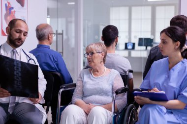 Steteskoplu doktor engelli yaşlı kadın radyografisi ile iletişim kuruyor.