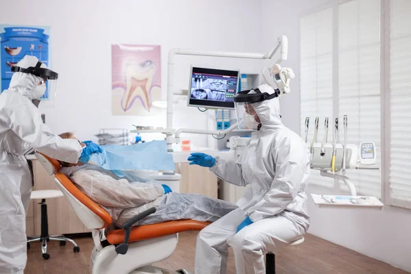 Медсестра-стоматолог измеряет температуру пациента в защитном костюме — стоковое фото