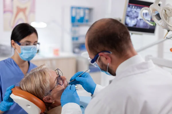 Стоматолог и медсестра лечат зубы пожилой женщины — стоковое фото