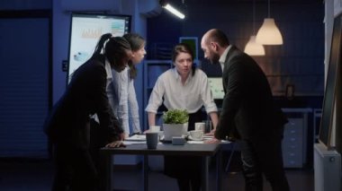 Çeşitli etnik gruplar, konferans masasının etrafında durmuş beyin fırtınası yapıyor.