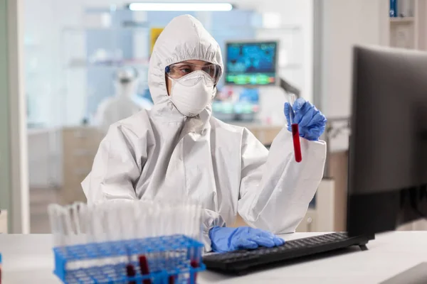 Pesquisador em coverall segurando tubos de ensaio com amostra de sangue para novo tratamento em laboratório médico. — Fotografia de Stock