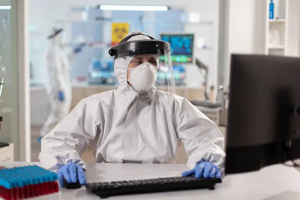 Scientifique vêtu d'une combinaison ppe travaillant sur ordinateur pour vaccin contre le virus — Photo