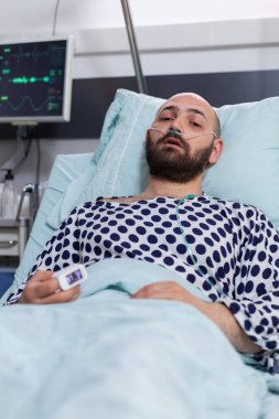 Burnunda oksijen tüpü olan üzgün hasta bir adam kameraya kötü bakıyor.