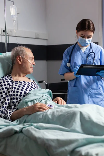 Medical assistant with protection mask checking treatment of senior man — Stock Photo, Image