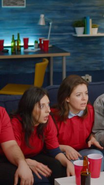 Çok uluslu arkadaşlar kanepede oturmuş futbol izliyorlar.