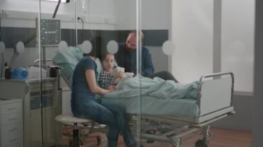 Endişeli ebeveynler hasta kız kızlarıyla oturup sağlık muayenesi sırasında hastalık uzmanlığını bekliyorlar.