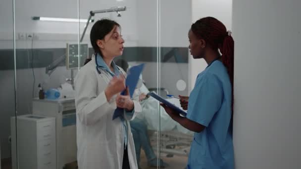 Врач-педиатр обсуждает симптомы болезни с африканской медсестрой, изучающей диагноз — стоковое видео
