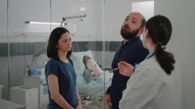 Endişeli ebeveynler hastane koğuşunda pediatri doktoruyla hastalık tedavisini tartışıyor.
