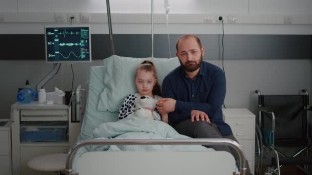 Szomorú apa portréja, amint beteg gyermek kezét fogja, miközben kamerába néz az orvosi konzultáció során. — Stock videók