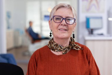 Diş bekleme odasında kameraya bakan yaşlı bir kadın.