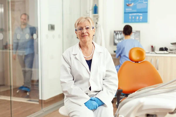 Ортодонт старший в медичній формі сидить на стільці, дивлячись в камеру — стокове фото