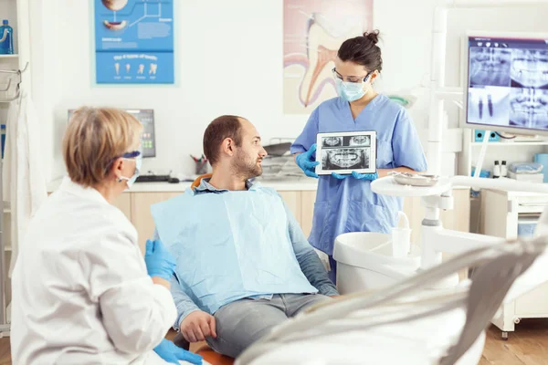 Больной человек сидит на стоматологическом стуле и слушает доктора — стоковое фото