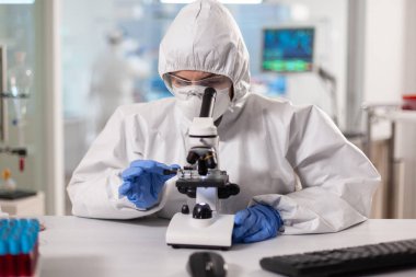 Pen giysili bilim adamları laboratuvar mikroskobuna bakıp ayarlamalar yapıyorlar.