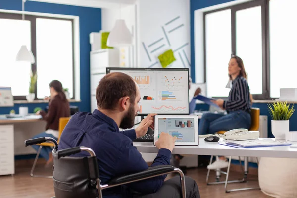 Handicapped man employee sitting in wheelchair working at notepad and computer — Stock Photo, Image