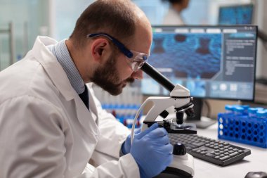 Erkek bilim adamı mikroskop altında virüs örneğine bakıyor