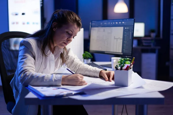 Femme architecte surmenée vérifiant et assortissant les plans assis au bureau — Photo