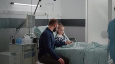 Hastanedeki muayene sırasında hasta kızın elini tutan bir baba.