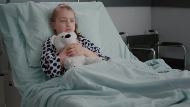 Yatakta elinde oyuncak ayıyla dinlenen oksijen tüpü takan endişeli çocuk hasta. — Stok video