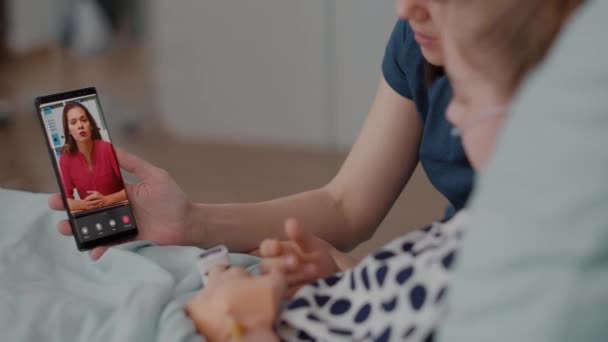Paziente malato che riposa a letto con mamma che saluta un amico remoto durante la conferenza di videocall online — Video Stock