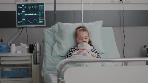 Портрет госпіталізованої хворої дитини, яка засинає, тримаючи плюшевого ведмедя в руках — стокове відео