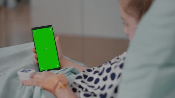 Beteg lány pihen az ágyban orvosi oximéterrel az ujján nézi zöld képernyő gúnyolódik chroma kulcs telefon — Stock videók