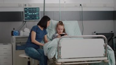 Anne hasta kızın yanında otururken çevrimiçi video oyunları ve oyun uygulaması oynuyor