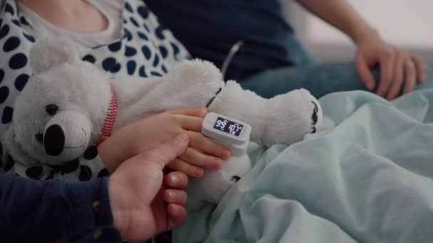 Крупным планом больная дочь отдыхает в постели с медицинским оксиметром на пальце — стоковое видео