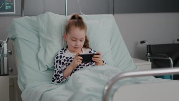Krankes kleines Kind ruht im Bett und spielt Online-Videospiele mit dem Smartphone — Stockvideo