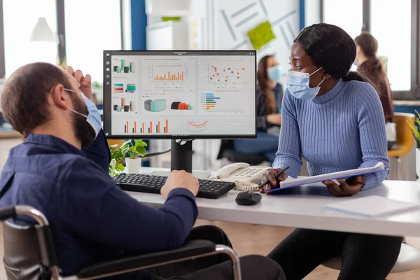 Paralysed freelancer with face mask discussing with black woman partner — Stock Photo, Image