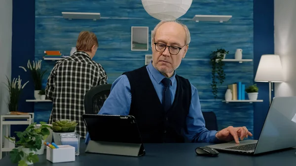 Elderly man using tablet and laptop in same time compering financial graphs — Stock Photo, Image